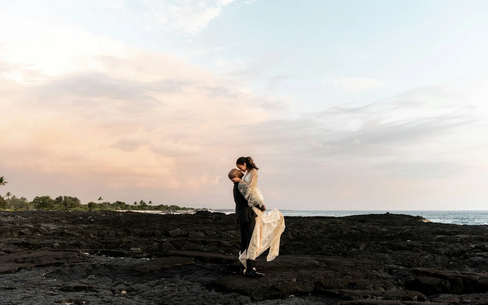 Couple embracing on a rocky coastline at dusk